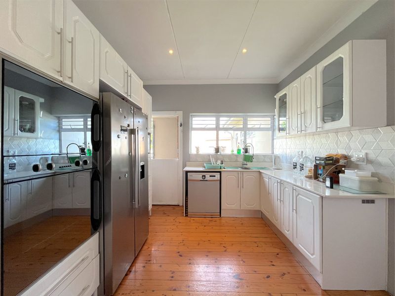 A well-maintained kitchen featuring white cabinetry, timber flooring, integrated oven, and a tiled backsplash with ample counter space.