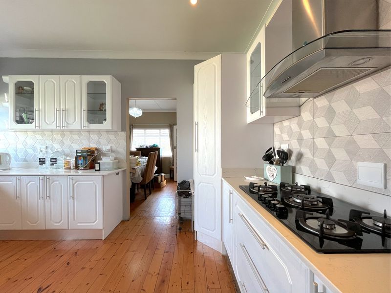 A well-maintained kitchen featuring white cabinetry, a gas hob with extractor fan, geometric tiled splashback, and warm timber flooring.