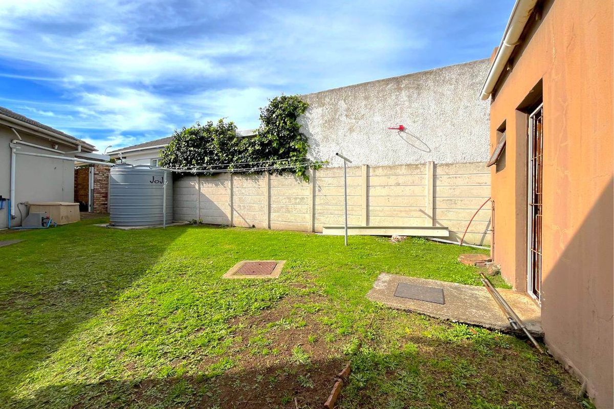 A rear garden area featuring a precast concrete boundary wall, a water storage tank, and a basic lawn space with a concrete apron.