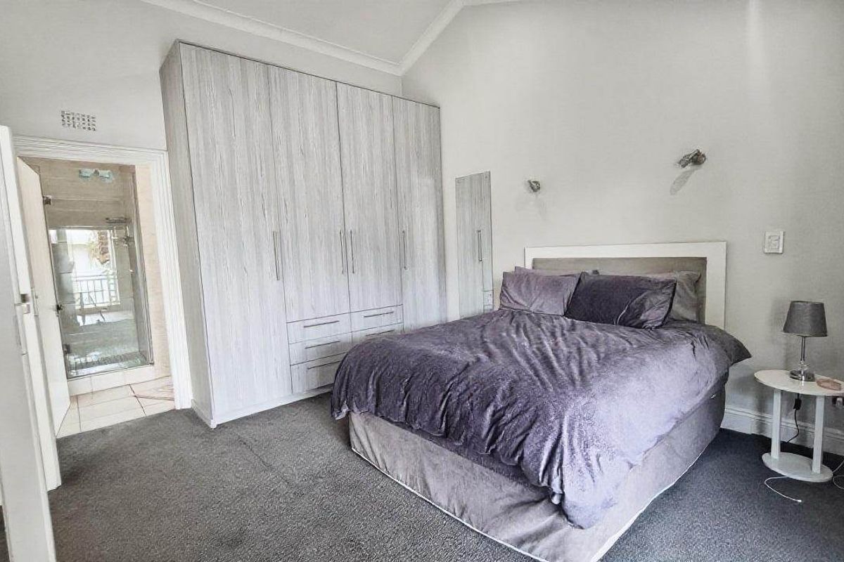 A well-maintained bedroom featuring built-in cupboards, carpeted flooring, and a vaulted ceiling, with direct access to an en-suite bathroom.