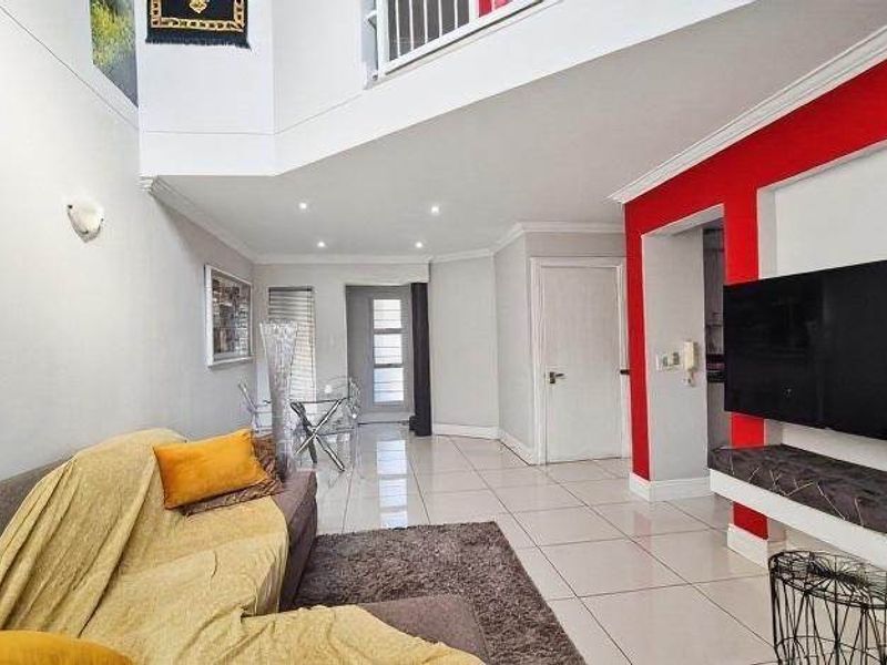Spacious open-plan living area featuring high ceilings, tiled flooring, recessed lighting, and a built-in media console with a mezzanine level above.