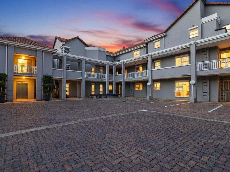 A well-maintained apartment complex courtyard featuring paved parking areas, multi-level balconies, and a classic tiled roof design at dusk.