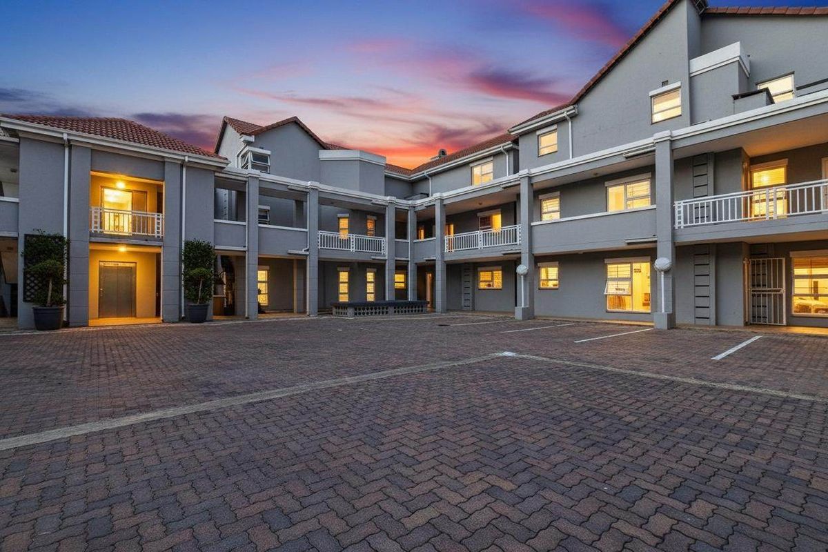 A well-maintained apartment complex courtyard featuring paved parking areas, multi-level balconies, and a classic tiled roof design at dusk.
