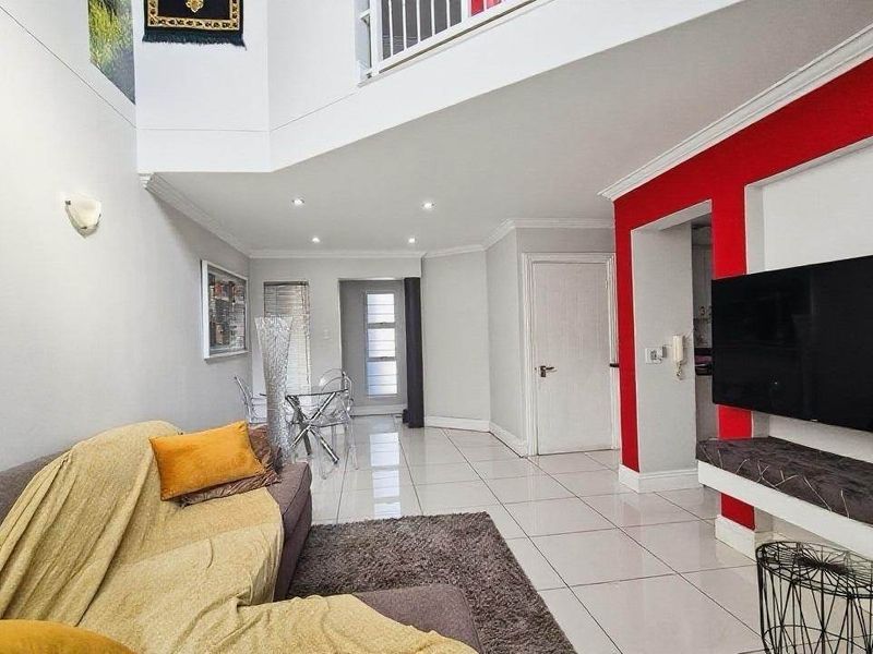 Spacious double-volume living area featuring sleek tiled flooring, recessed lighting, and a built-in media console with a striking red accent wall.