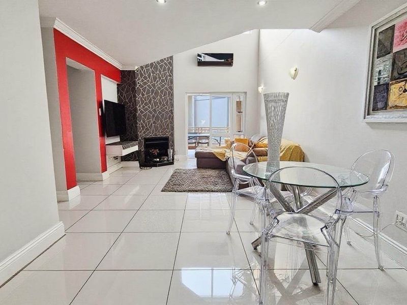 Spacious open-plan living and dining area featuring tiled floors, a fireplace, and high vaulted ceilings with access to an outdoor balcony.