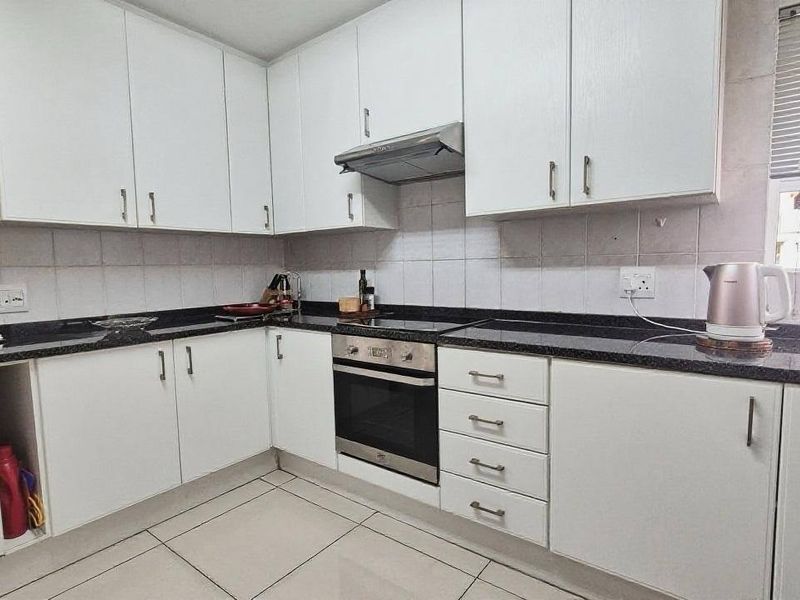A functional kitchen featuring white cabinetry, dark granite countertops, built-in oven and hob, and tiled flooring.