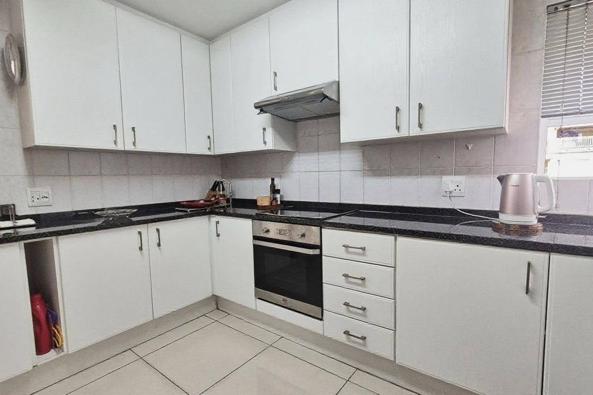 A functional kitchen featuring white cabinetry, dark granite countertops, built-in oven and hob, and tiled flooring.