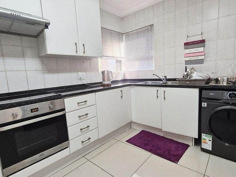 A functional kitchen featuring white cabinetry, granite countertops, a built-in oven with extractor fan, and tiled finishes throughout.