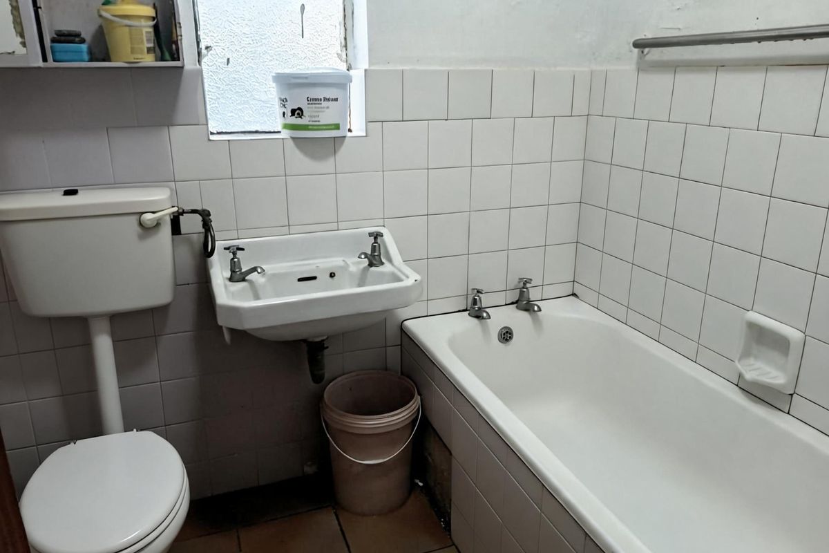 A dated bathroom featuring a standard bathtub, wall-mounted basin, and flush toilet with original ceramic wall tiling.