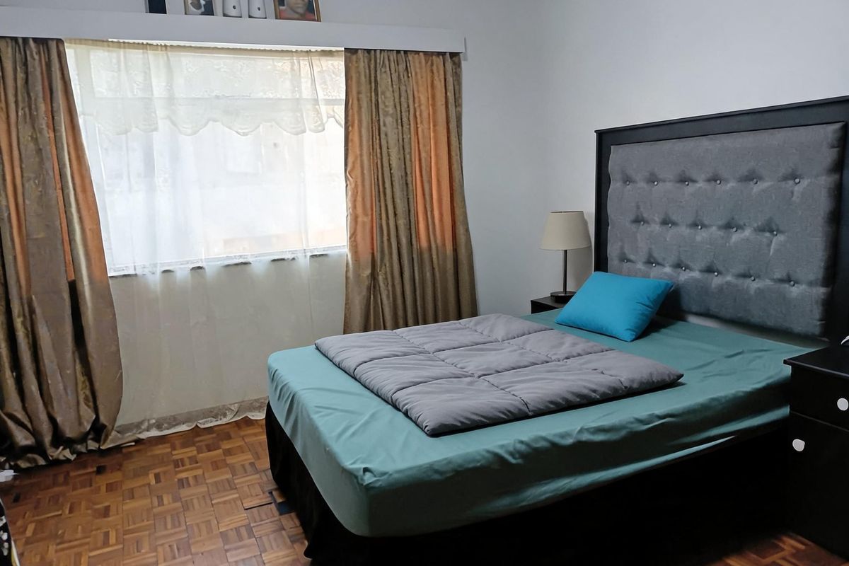 A bedroom featuring classic parquet flooring and a large window with installed curtain rods.