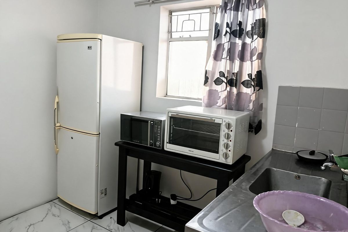 A functional kitchen area featuring tiled flooring, a stainless steel sink, and a window with security bars.