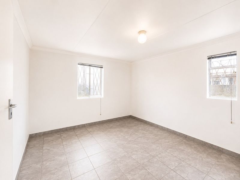 A clean, empty bedroom featuring neutral tiled flooring, white walls, and windows fitted with security bars.