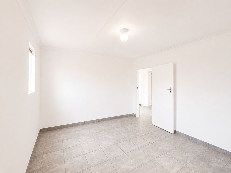 A clean, vacant bedroom featuring neutral tiled flooring, white walls, and a simple ceiling light fixture, offering a blank canvas for personalization.