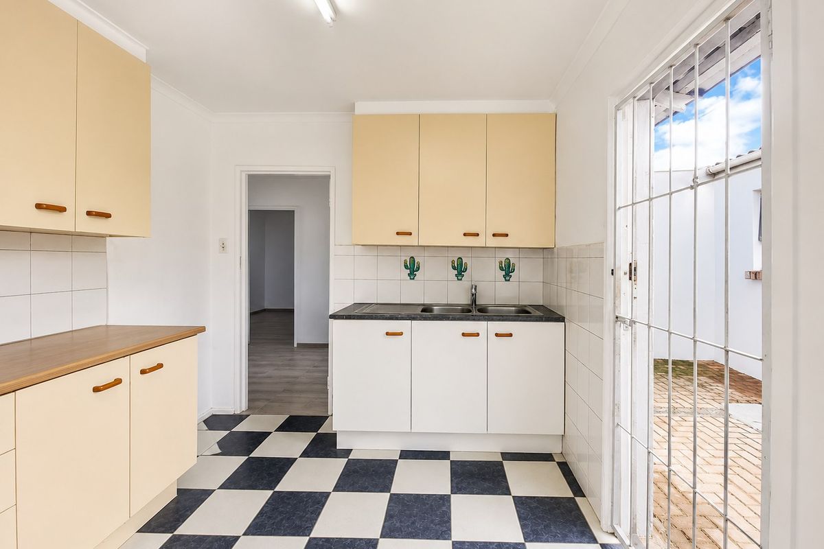 A functional kitchen featuring built-in cabinetry, laminate countertops, a double bowl sink, and direct access to an outdoor area through a security gate.