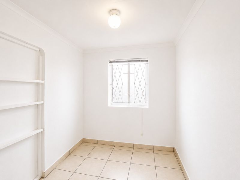 A clean, empty bedroom featuring neutral tiled flooring, built-in shelving, and a window fitted with security bars.