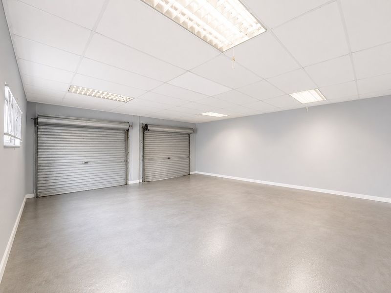 Spacious, clean garage area featuring dual roller shutter doors, durable epoxy flooring, and bright recessed lighting, suitable for vehicle storage or a workshop.