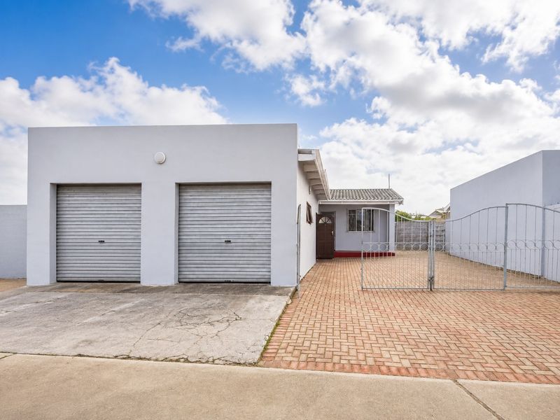 Front exterior view of the property featuring a double garage with roller shutter doors, a paved driveway, and a secure metal gate entrance.