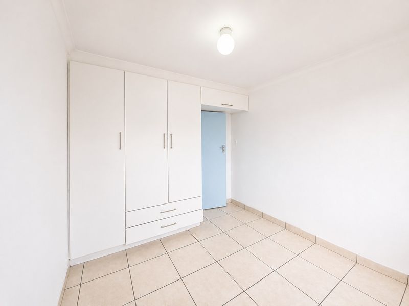 A clean, empty bedroom featuring neutral tiled flooring, white walls, and a built-in wardrobe with integrated storage.
