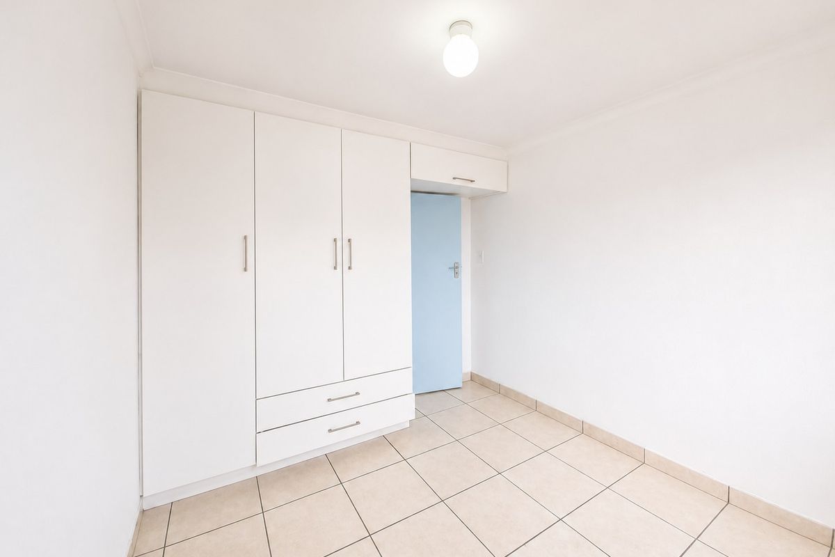 A clean, empty bedroom featuring neutral tiled flooring, white walls, and a built-in wardrobe with integrated storage.