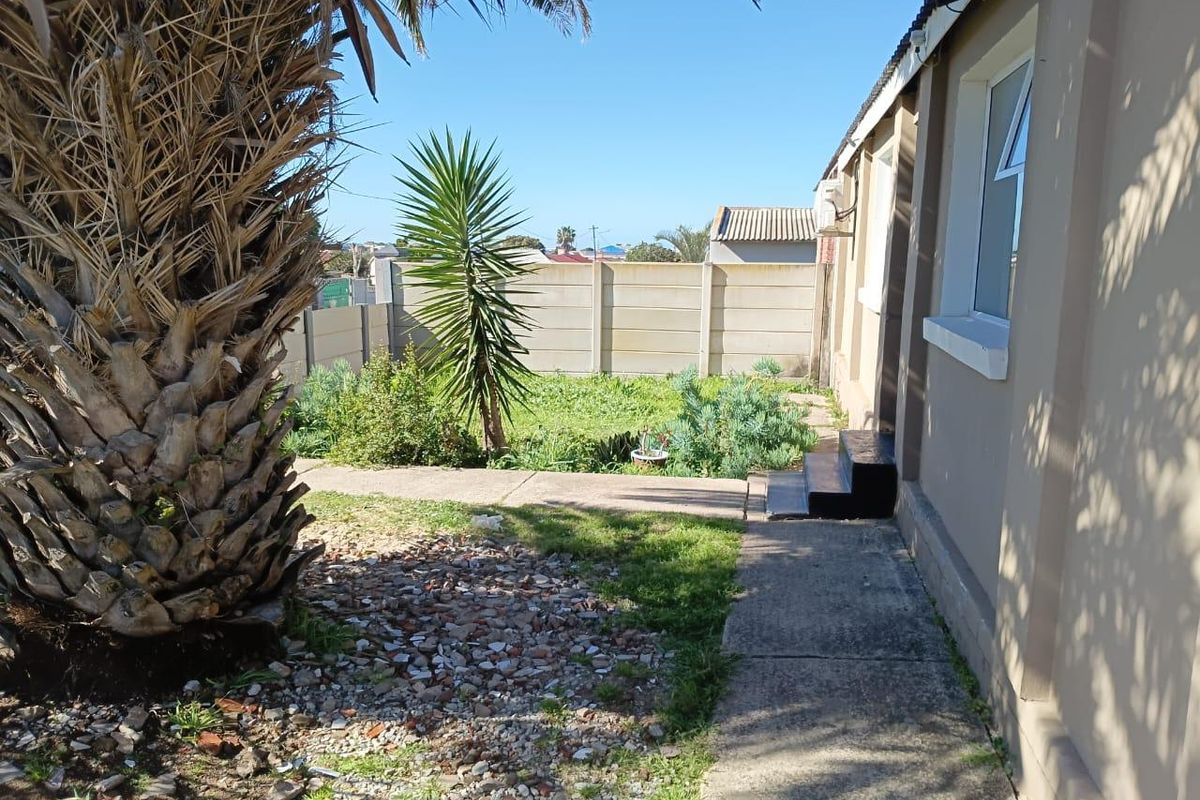 Rear exterior view of the property featuring a concrete pathway, boundary wall, and garden area requiring maintenance.