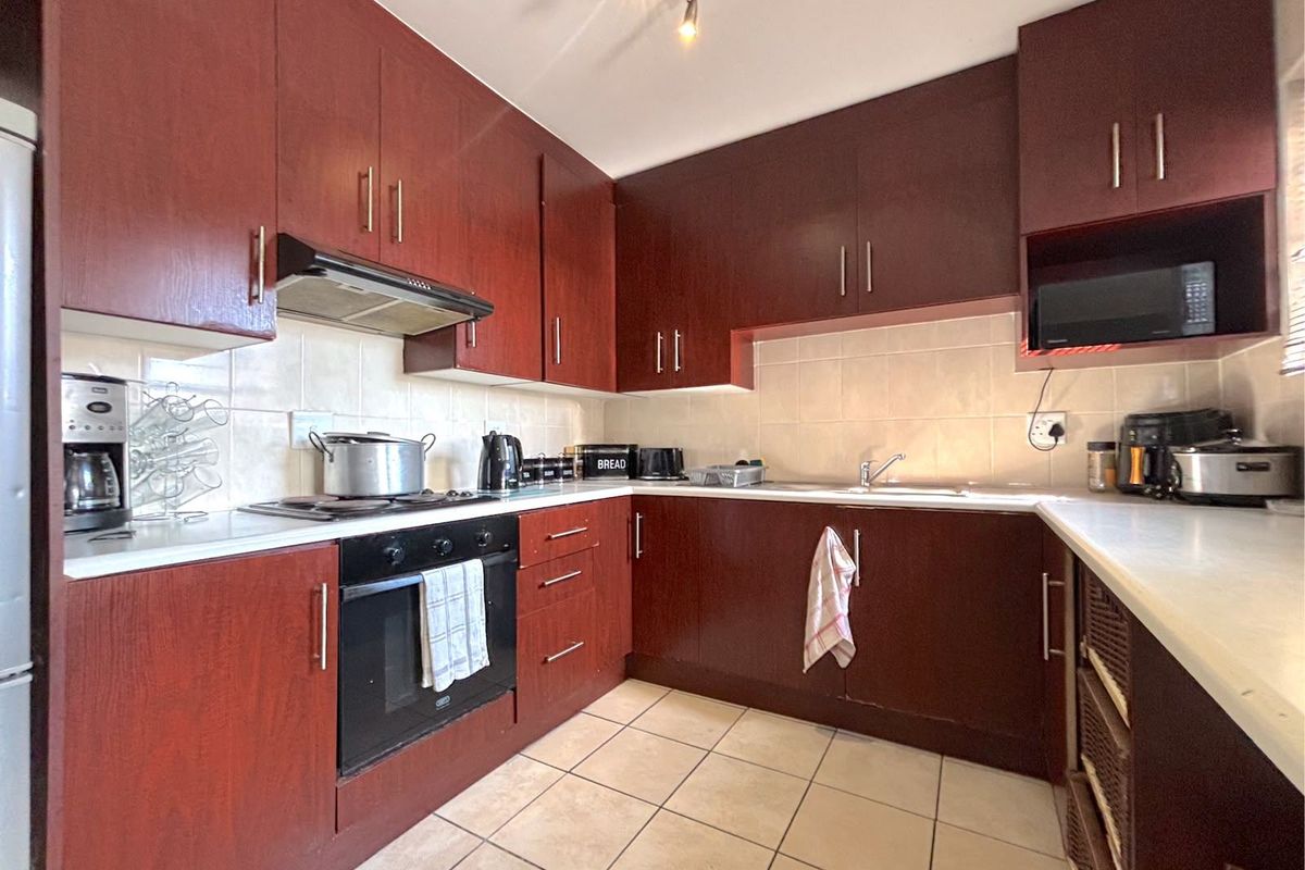 A functional kitchen featuring dark wood-finish cabinetry, laminate countertops, ceramic tile backsplash, and integrated appliances including an oven and hob.