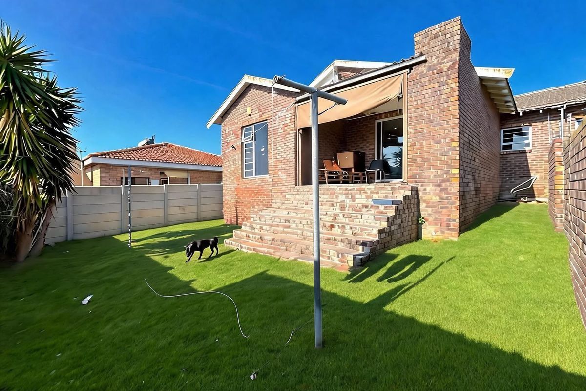 Rear view of a brick house featuring a raised patio area with a retractable awning, brick staircase, and a private lawn with boundary walling.