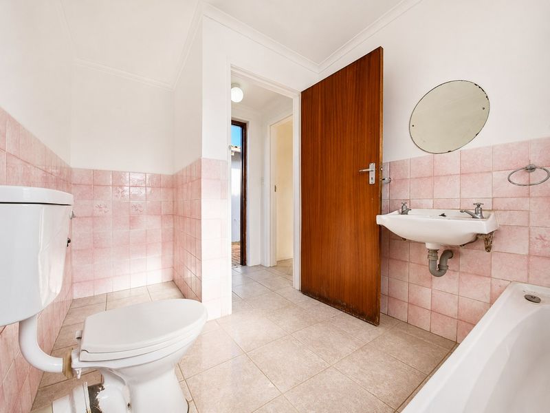 A dated bathroom featuring pink wall tiles, a pedestal basin, bathtub, and toilet, offering a blank canvas for a modern renovation.