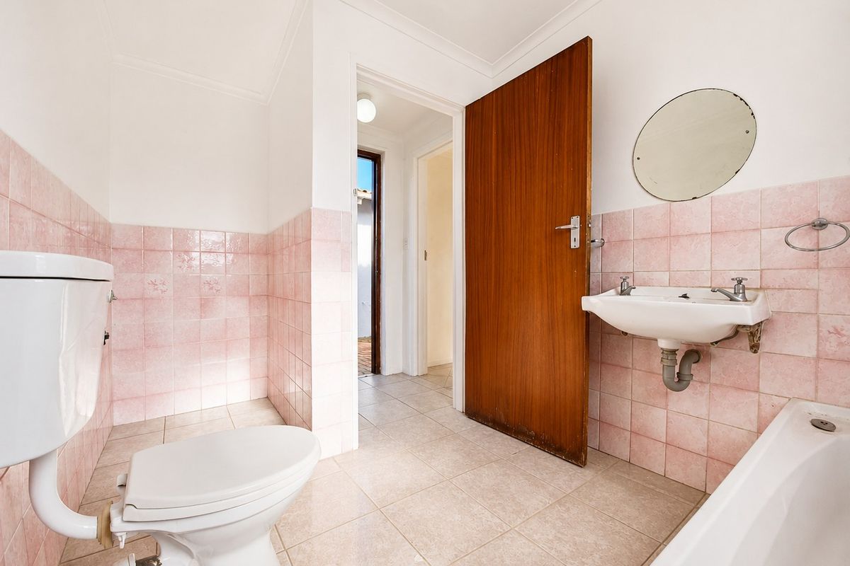 A dated bathroom featuring pink wall tiles, a pedestal basin, bathtub, and toilet, offering a blank canvas for a modern renovation.