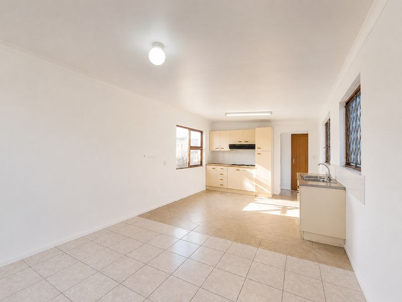 A functional, empty kitchen featuring light-toned cabinetry, tiled flooring, a built-in hob with extractor fan, and a stainless steel sink.