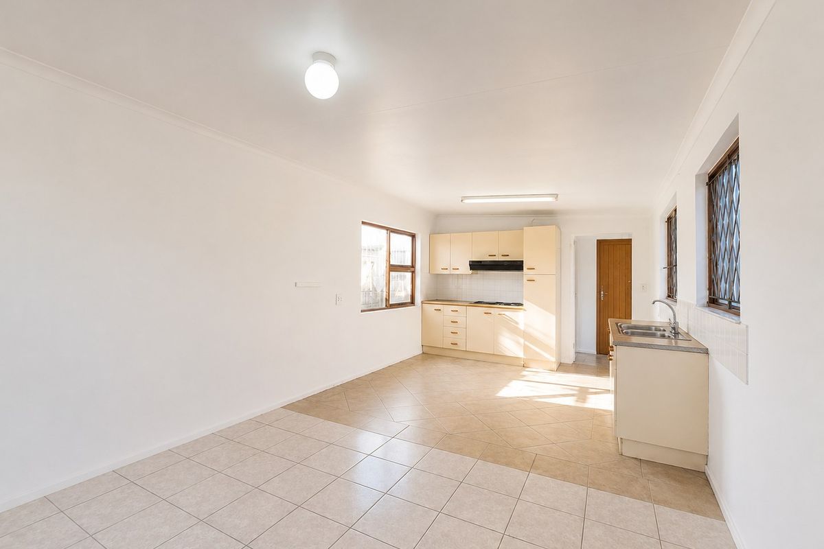 A functional, empty kitchen featuring light-toned cabinetry, tiled flooring, a built-in hob with extractor fan, and a stainless steel sink.