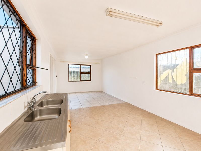 An empty, functional kitchen area featuring tiled flooring, a stainless steel double sink, and security bars on the windows.