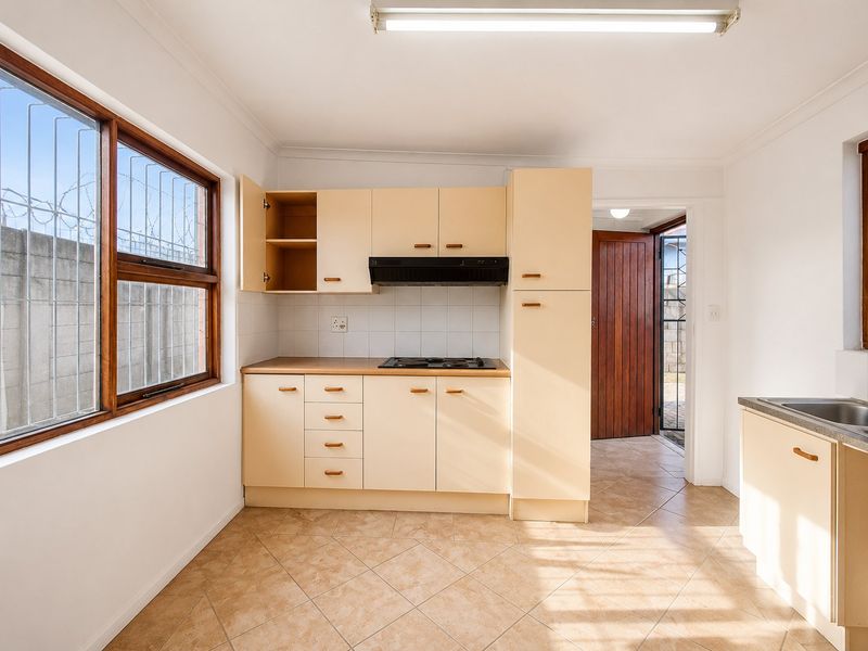 A functional kitchen featuring built-in cabinetry, a hob with extractor fan, tiled flooring, and a stainless steel sink, offering potential for modern updates.