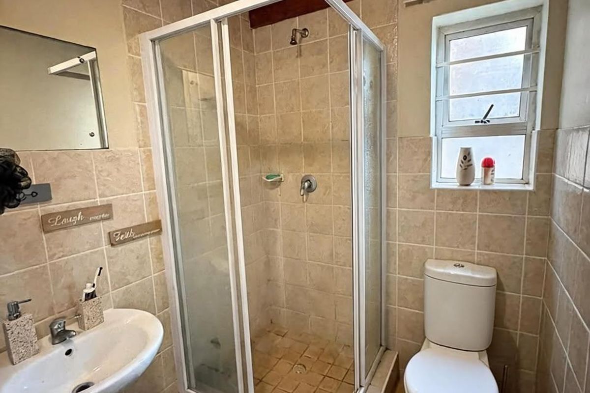 A compact bathroom featuring a pedestal basin, shower enclosure, toilet, and rustic exposed timber ceiling beams with tiled finishes throughout.