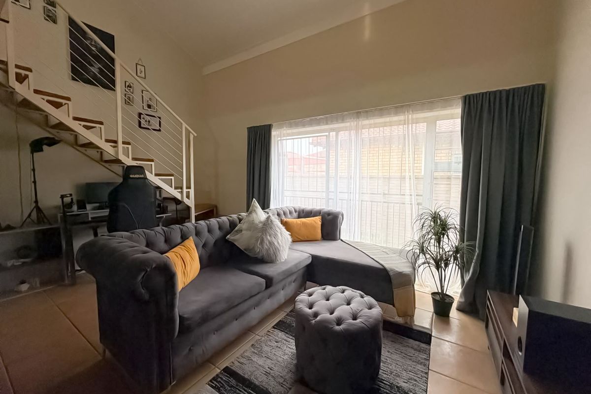 A bright living room featuring high ceilings, tiled flooring, and a staircase leading to an upper level, with access to an outdoor area.