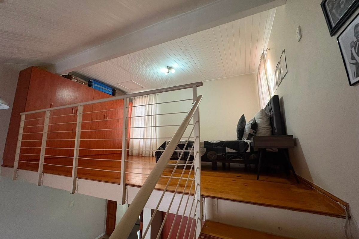 A mezzanine bedroom level featuring warm timber flooring, built-in storage cabinetry, and a protective metal balustrade overlooking the lower living area.