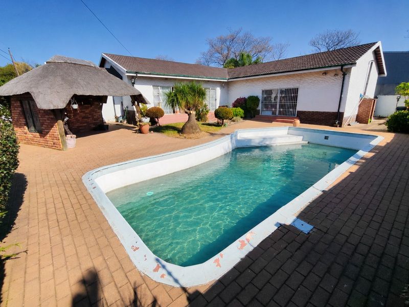 Outdoor entertainment area featuring a swimming pool, brick-paved patio, and a traditional thatched lapa structure.