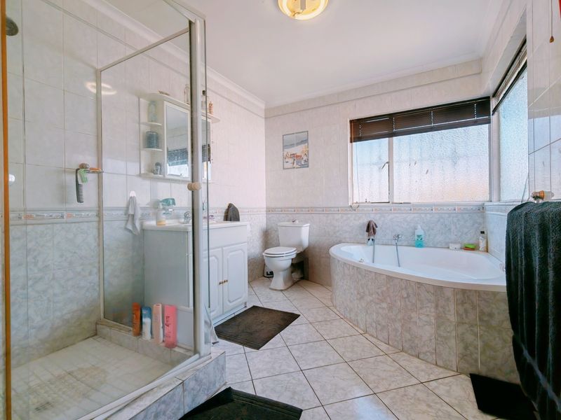 A spacious bathroom featuring a glass shower enclosure, a built-in bathtub, a vanity cabinet, and a toilet, finished with neutral wall and floor tiles.