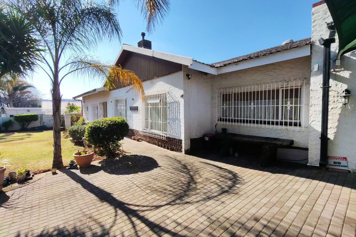 Rear exterior view of the house featuring a paved patio area, security bars on windows, and a textured facade.