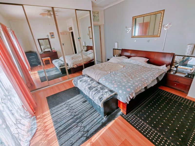 A well-lit bedroom featuring laminate flooring and a large built-in mirrored wardrobe, providing ample storage and reflecting natural light throughout the space.