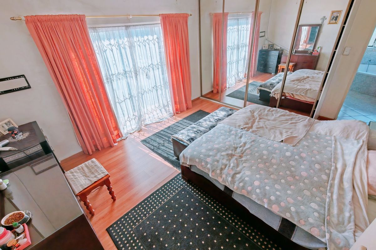 Spacious bedroom featuring laminate flooring, large sliding mirror wardrobe doors, and direct access to an outdoor area through sliding glass doors.