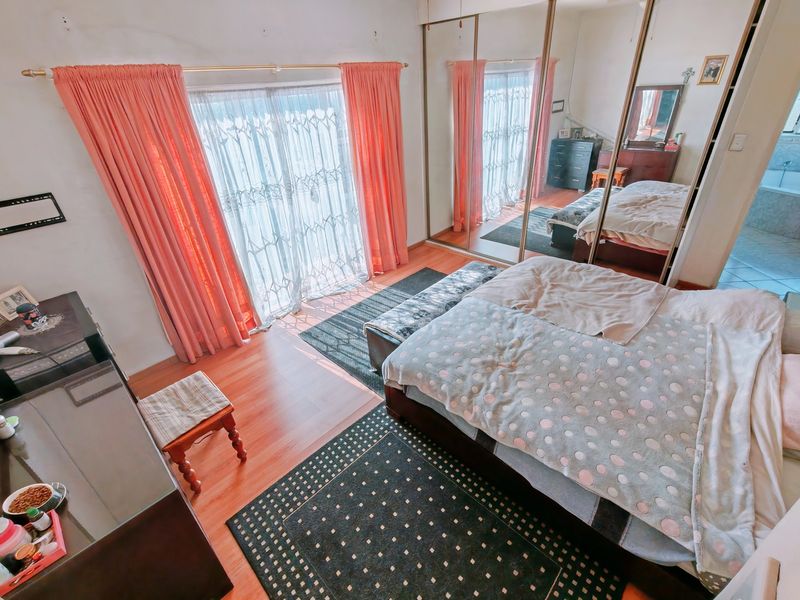 Spacious bedroom featuring laminate flooring, large sliding mirror wardrobe doors, and direct access to an outdoor area through sliding glass doors.