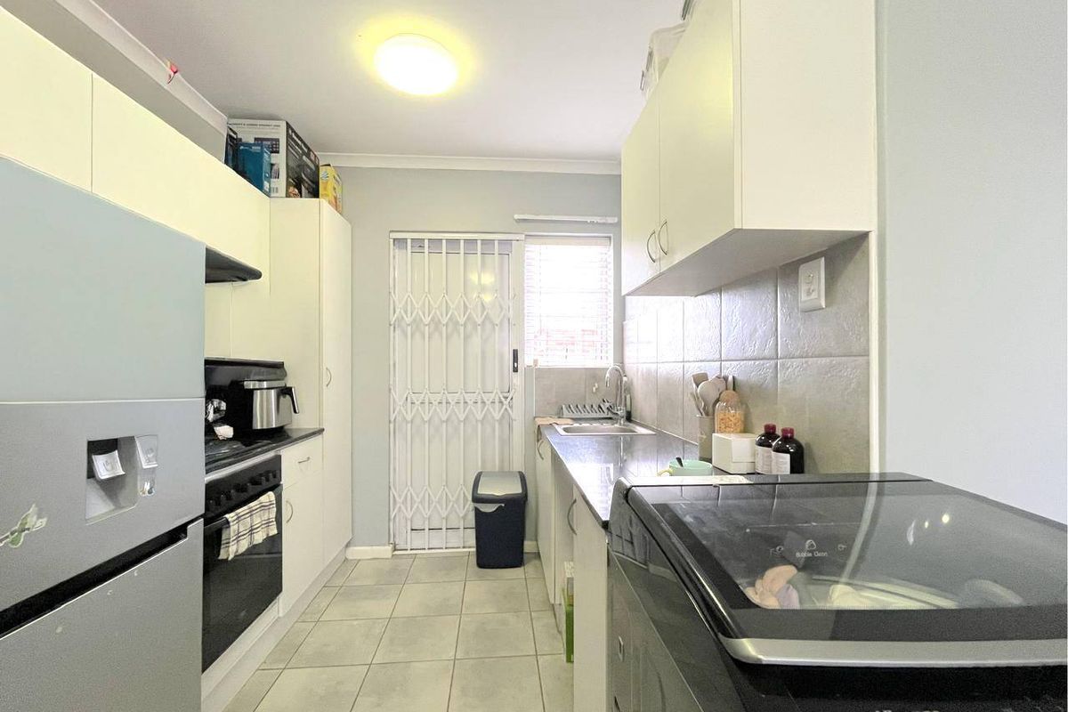 Functional kitchen featuring built-in cabinetry, laminate countertops, tiled backsplash, and direct access to the exterior via a security gate.