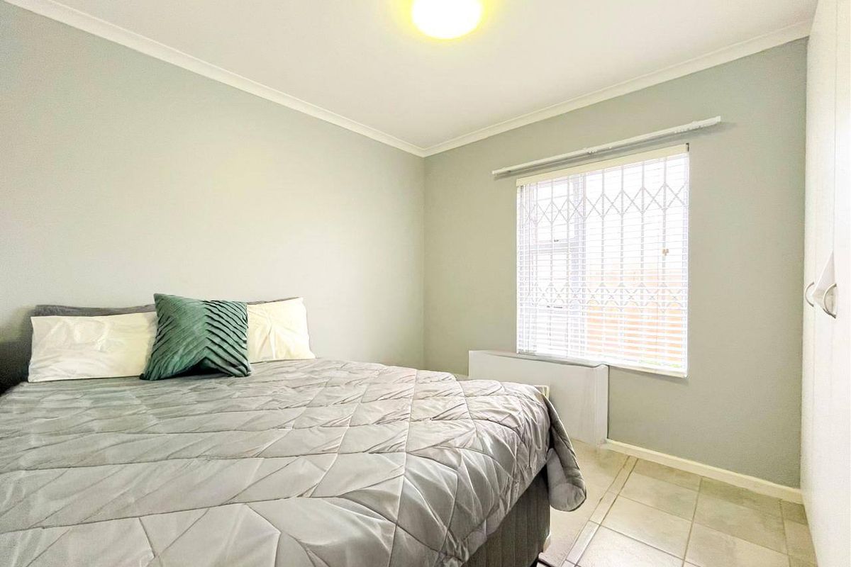 A functional bedroom featuring tiled flooring, a built-in wardrobe, and a window fitted with security bars.