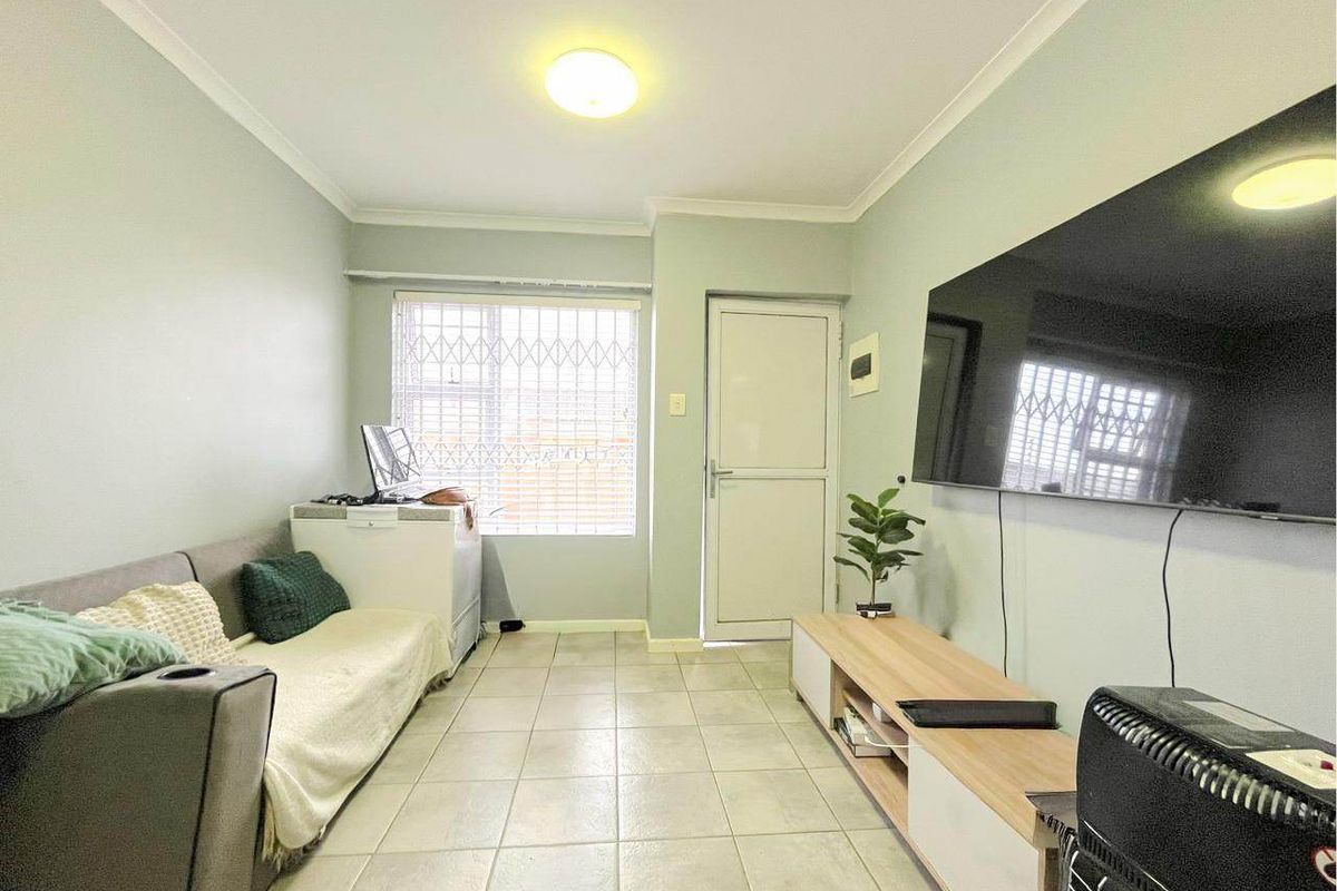 A functional living room featuring tiled flooring, a security gate on the exterior door, and neutral wall finishes.