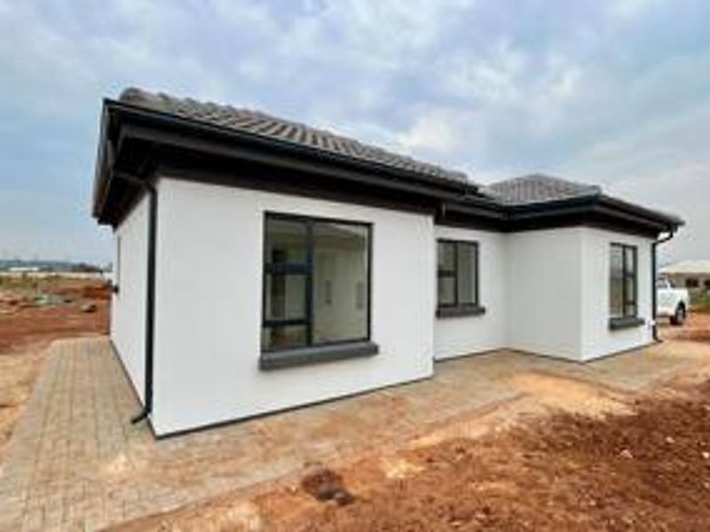 A modern single-story house exterior featuring white rendered walls, dark aluminium window frames, a tiled roof, and a paved perimeter walkway.