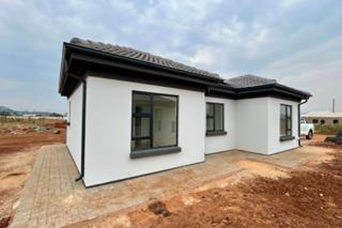 A modern single-story house exterior featuring white rendered walls, dark aluminium window frames, a tiled roof, and a paved perimeter walkway.