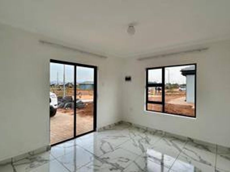 A bright, empty living room featuring modern marble-look porcelain floor tiles and black aluminium window and door frames.
