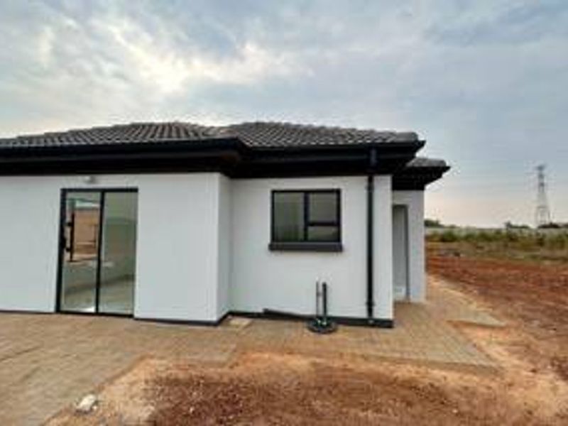 Rear view of a modern house featuring a paved patio area, sliding glass doors, and clean white exterior finishes.