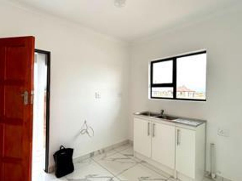 A clean, empty scullery area featuring modern white cabinetry, a stainless steel sink, and tiled flooring, providing a functional space for utility tasks.