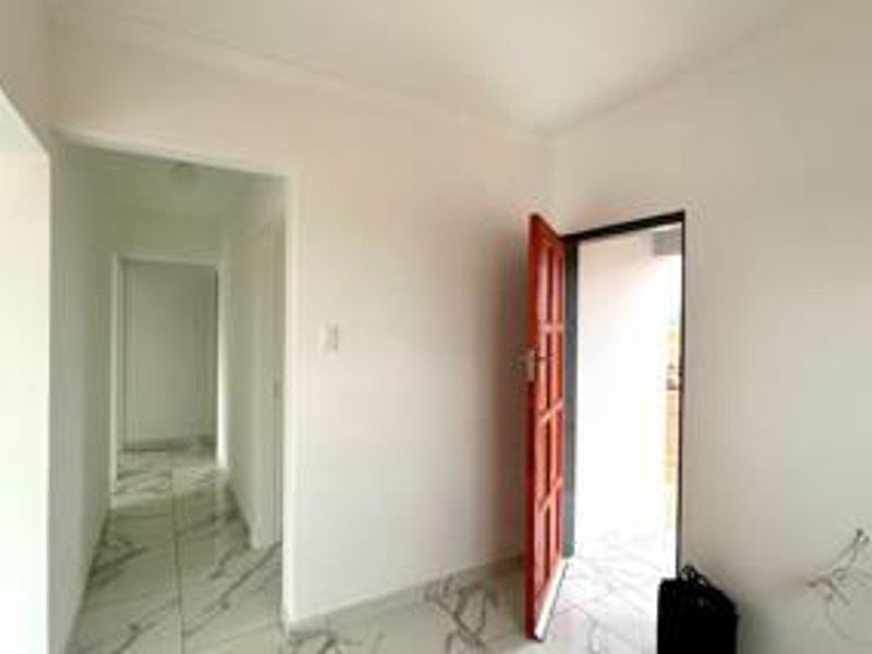 A bright and clean entrance area featuring modern marble-look floor tiles and a classic timber door leading to the exterior.